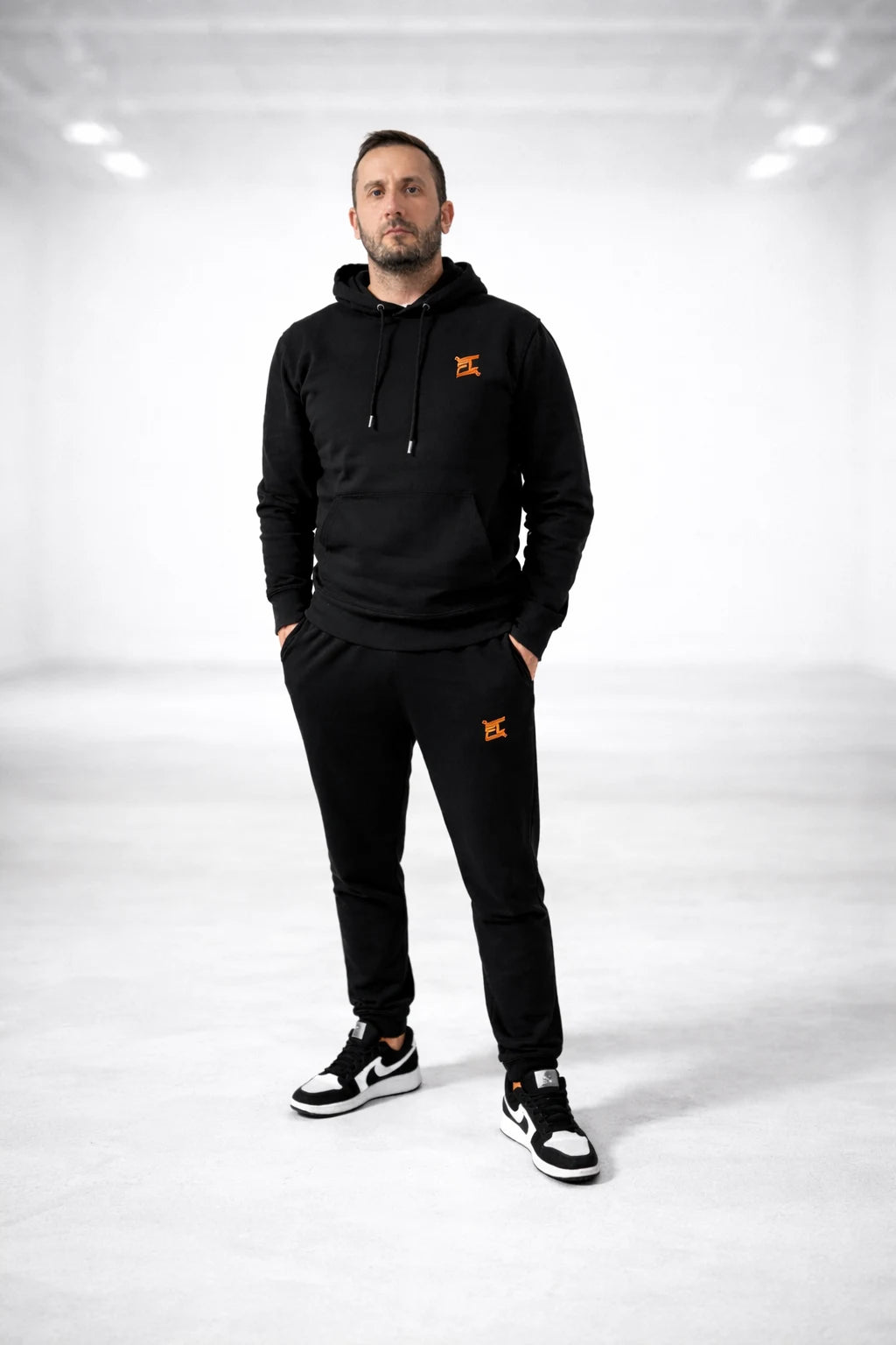 Homme portant l'ensemble noir causal de la marque FL-FIT avec le logo brodée FL de couleur orange un style décontracté 