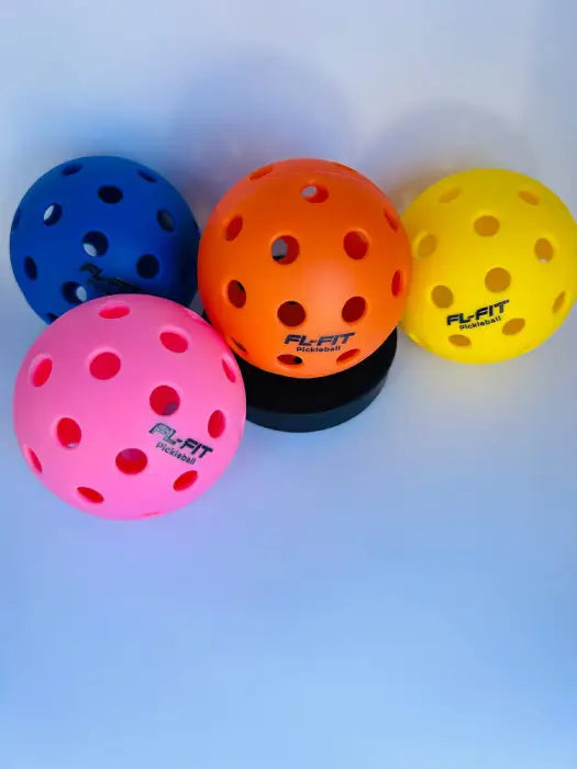 Balle de pickleball mulicouleur FL-FIT avec trous sur socle noir, fond bleu clair