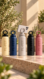 Cinq gourdes isothermes FL-FIT 1L en acier inoxydable, coloris crème, bleu marine, gris, noir et rose, avec support téléphone intégré, présentées au soleil.